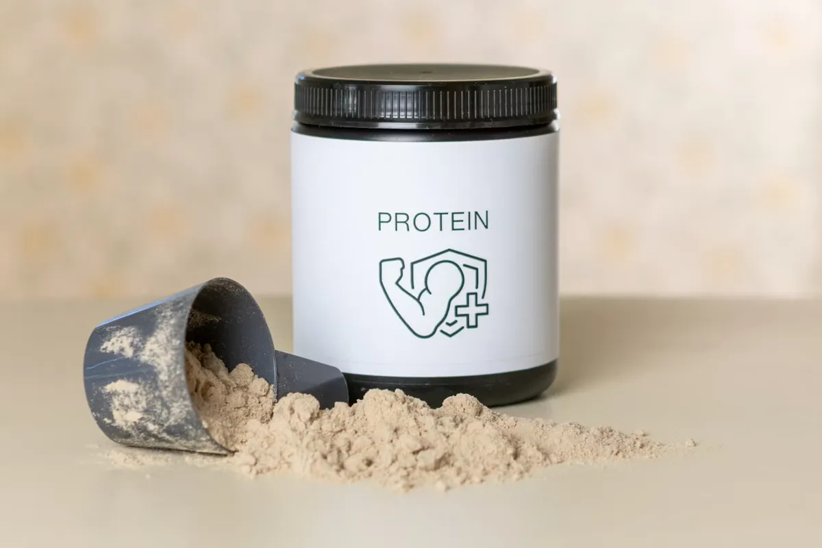 Bote de proteína en polvo con un scoop de suplemento derramado sobre la mesa
