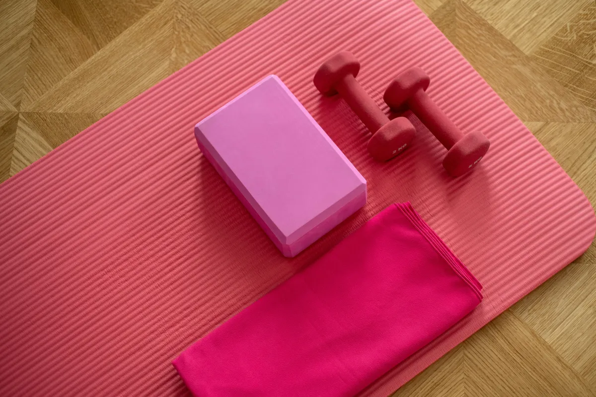 Mancuernas, bloque de yoga y toalla sobre una esterilla rosa